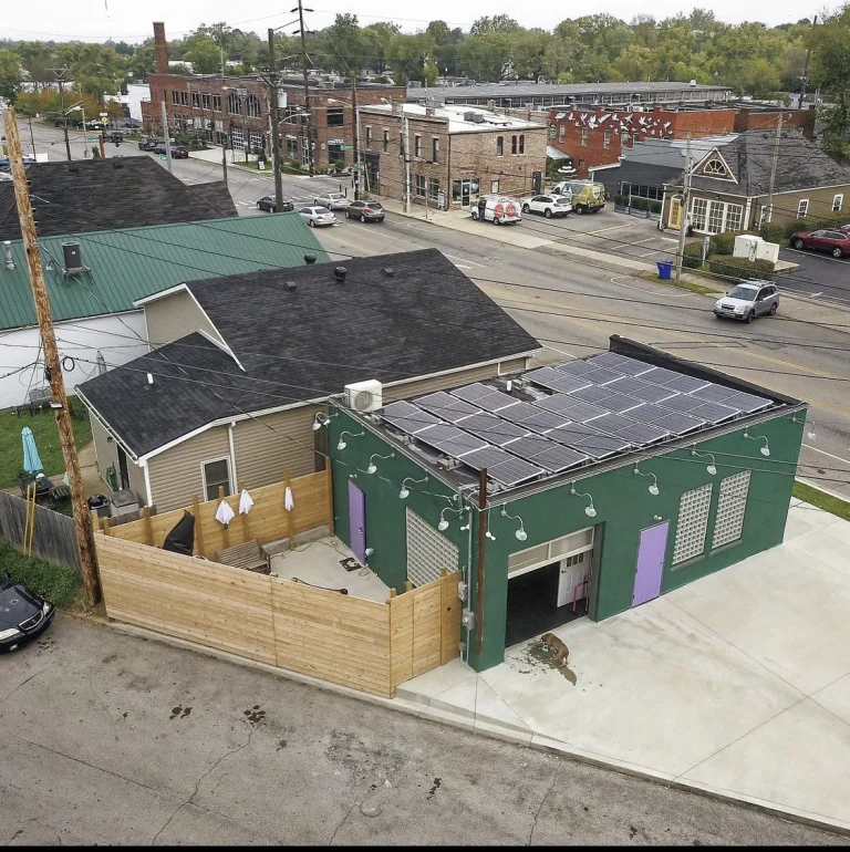 An aerial view of the green studio building with its purple doors, solar panels and fenced patio, on the corner in Lexington