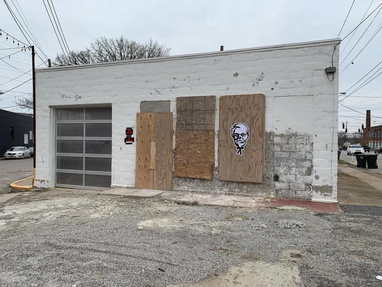 The boarded-up white block building the studio was built from, with graffiti on the plywood