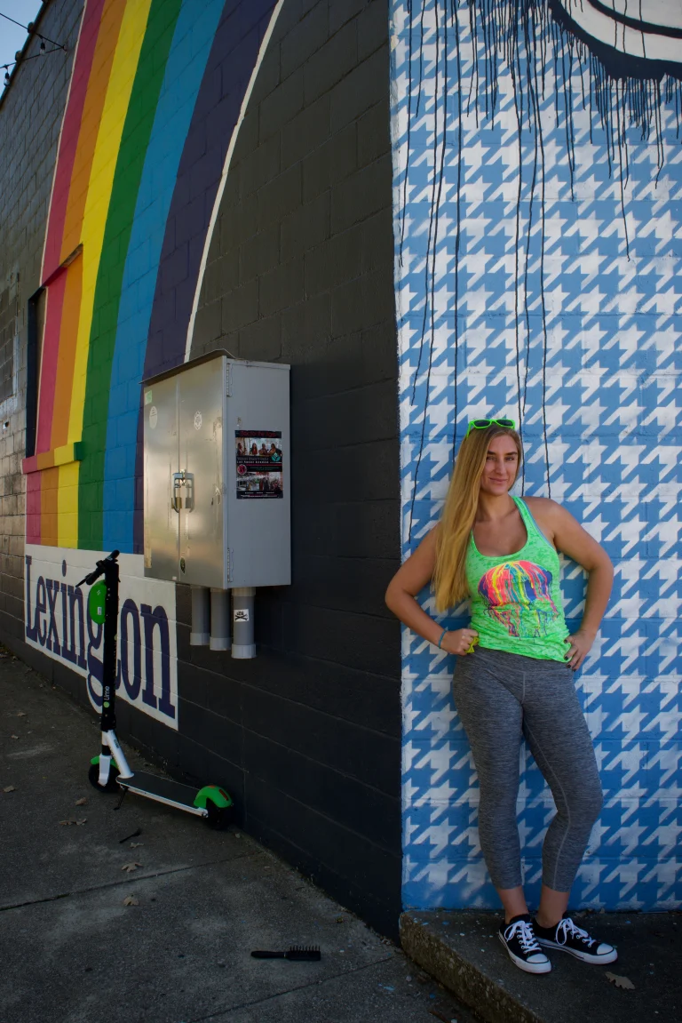 Ivy standing with one hand on her hip against a blue and white houndstooth mural beside the Lexington rainbow