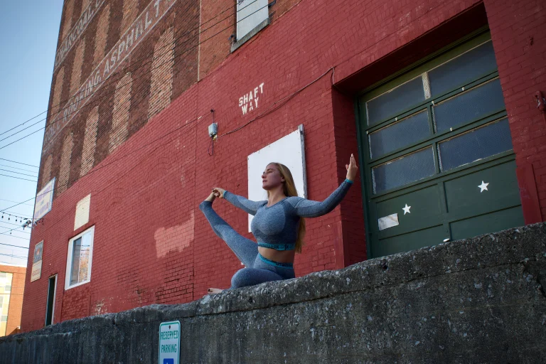 Ivy in a seated pose on a concrete ledge in front of a red brick warehouse with a painted green loading door
