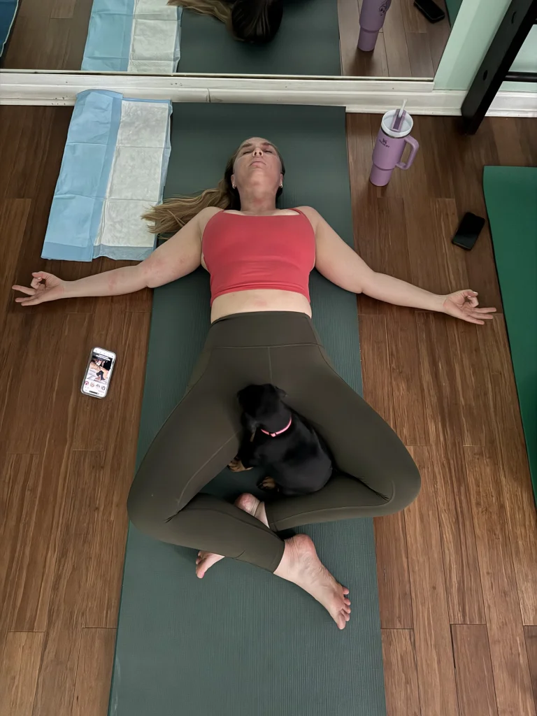 A student in savasana with a small dog in her lap
