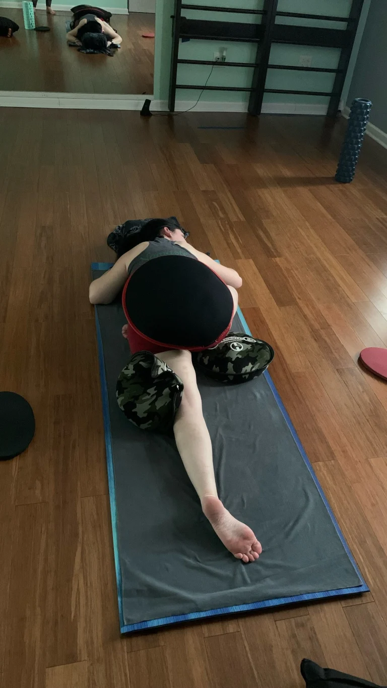 A student in a deep forward stretch on a mat in the studio