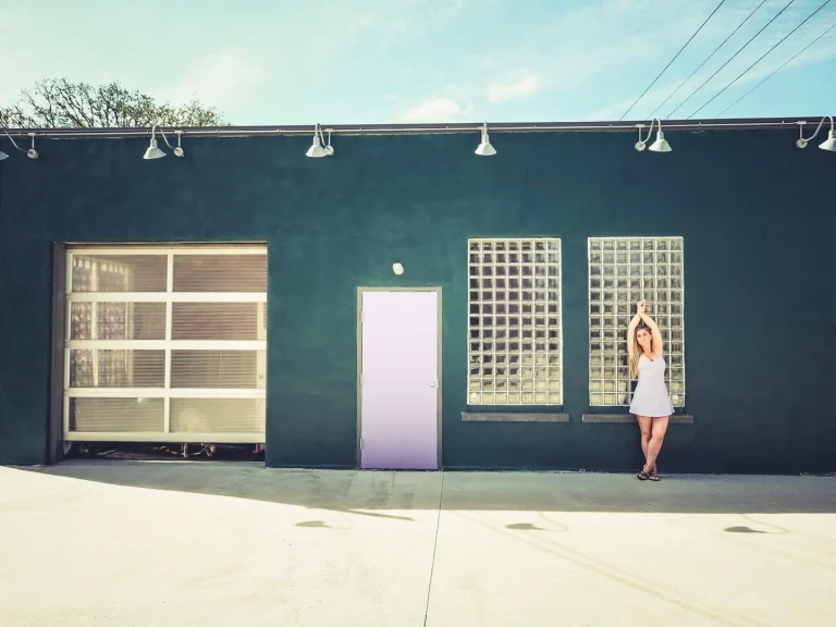 The studio's green front wall in daylight with the roll-up door, the purple entrance door and two glass block windows, and Ivy standing at the right