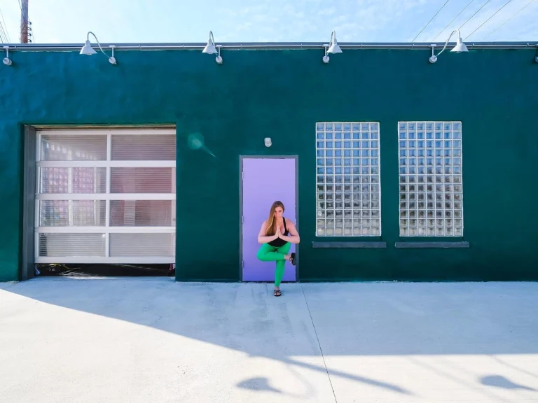 Ivy balanced on one leg in the studio's open purple doorway, framed by the green wall, the roll-up door and the glass block windows