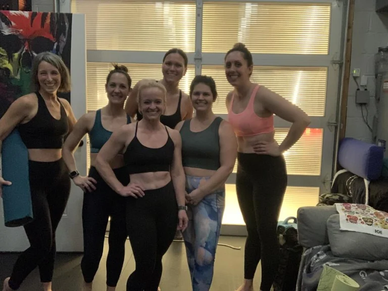 Six students standing together and smiling after class in front of the studio's lit roll-up door
