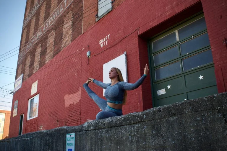 Ivy in a seated pose on a concrete ledge in front of a red brick warehouse with a painted green loading door