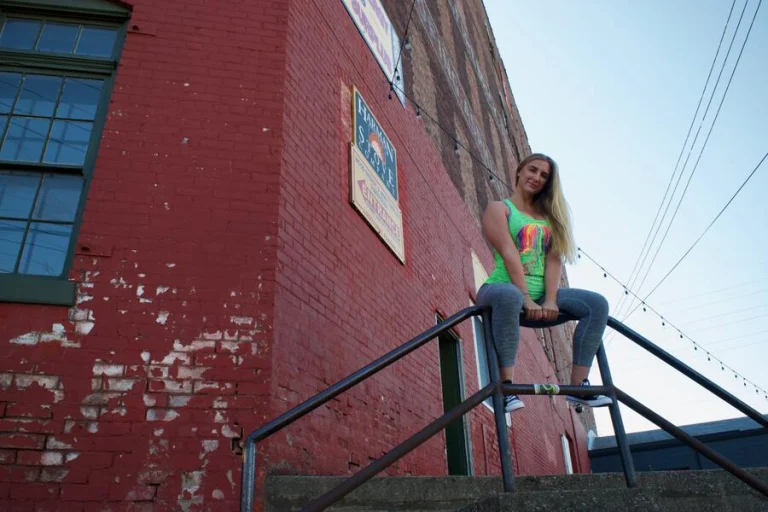 Ivy sitting on a stair handrail in front of a red brick wall with a painted Harmony Stove sign
